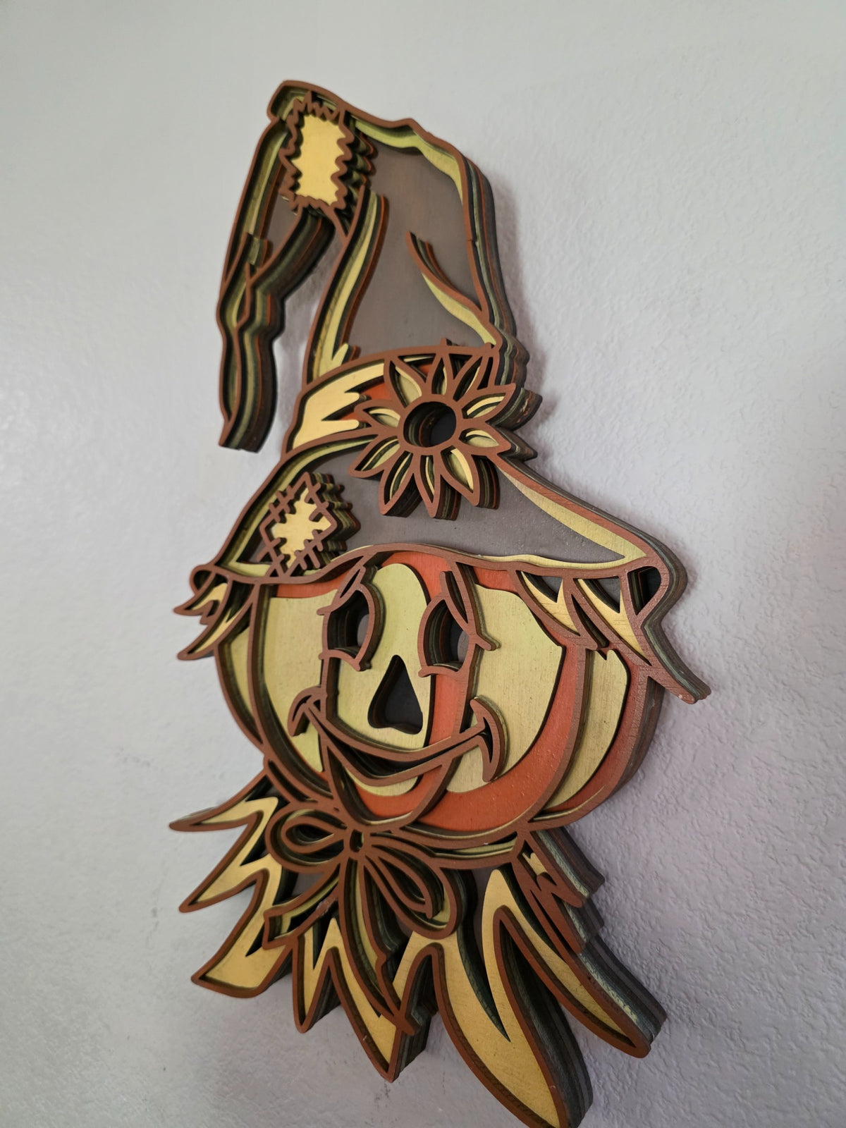Angled side view of layered wooden scarecrow pumpkin with witch hat and sunflower