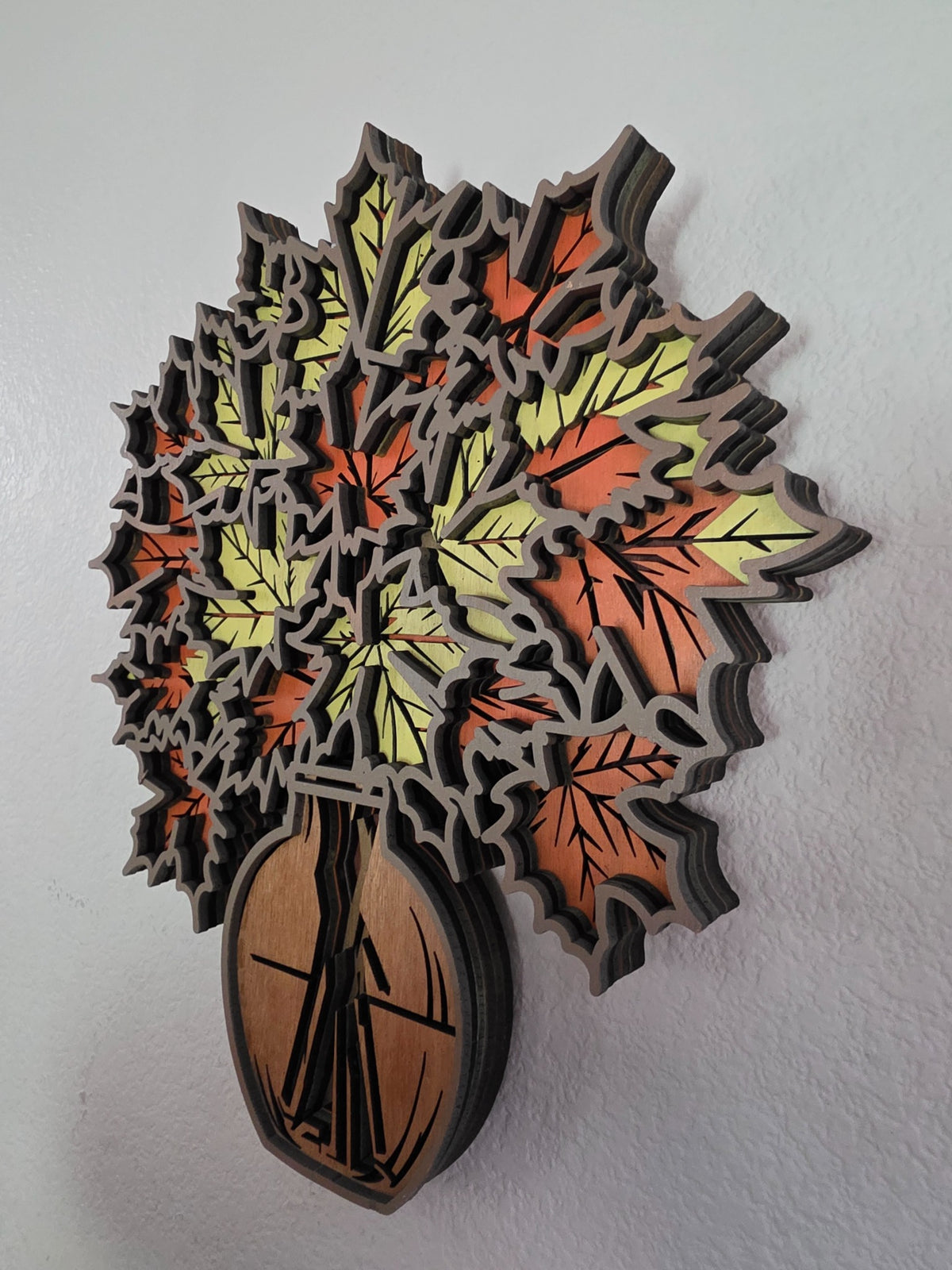 Angled view of layered wooden maple leaf bouquet and vase wall art showing dimensional stacked wood layers