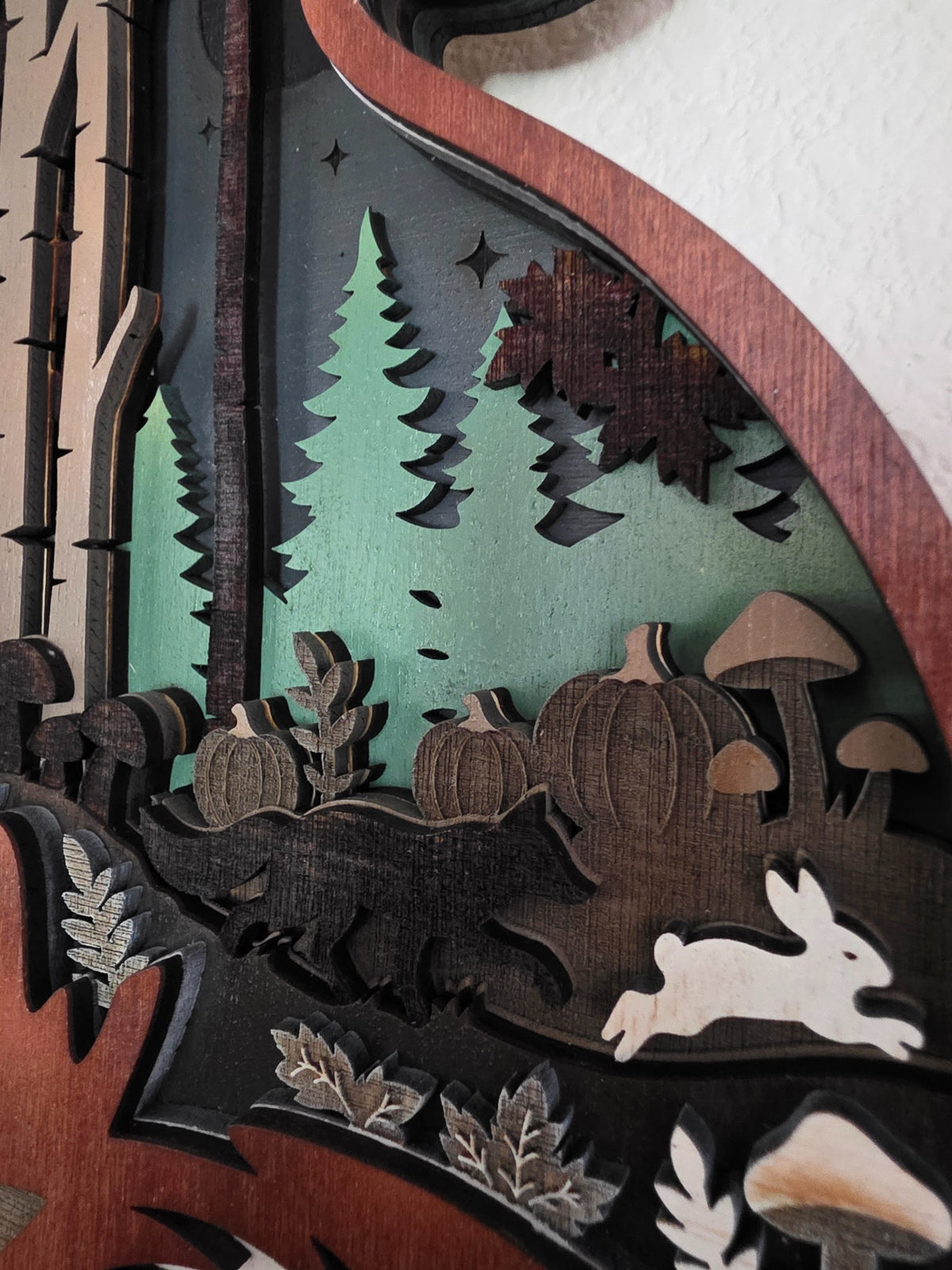 Close-up detail of pine trees, pumpkins, mushrooms, rabbit, and layered woodland scene inside fox silhouette